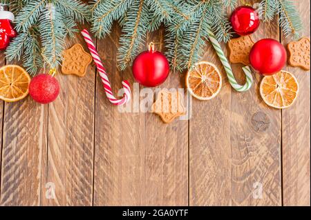 Rami di abete natalizio con baubles, canne caramelle, arance secche e biscotti a forma di stella su sfondo di legno con spazio di copia. Foto Stock