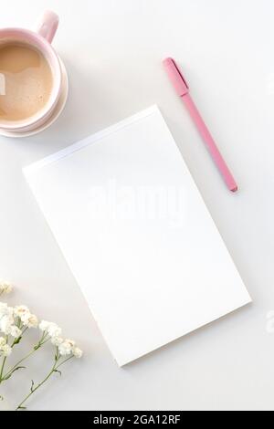 Piano di lavoro con scrivania con notebook aperto, penna rosa, caffè e fiori di gypsophila Foto Stock