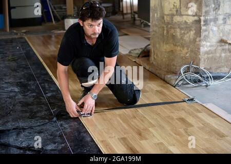 Impostazione del morsetto di compressione da parte dell'operatore su una linguetta di legno laminata e un pavimento con scanalatura appena installati Foto Stock