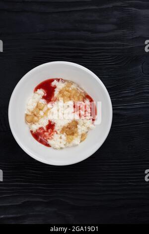 Porridge di latte di riso con marmellata di fragole e mela in piatto bianco su fondo di legno nero Foto Stock