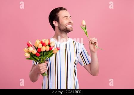 Foto ritratto uomo in t-shirt sorridente godendo odore tulipano fiori isolato colore rosa pastello sfondo Foto Stock