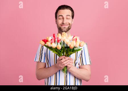 Foto di sognante giovane felice uomo affascinante odore fiori buon umore sorriso isolato su sfondo color rosa pastello Foto Stock