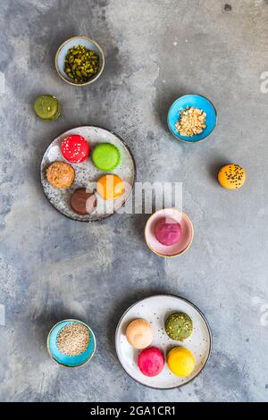 Macaron e ciotole colorati con guarnizioni su fondo grigio in cemento Foto Stock