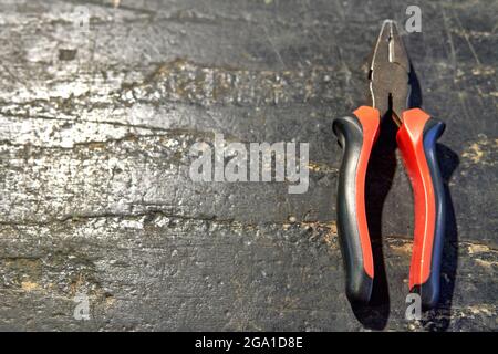 pinza isolata rossa e nera su fondo di legno. utensile, orizzontale e spazio di copia Foto Stock