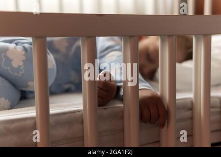 Carino piccolo allegro 2-3 anni prescolare bambino ragazzo dormire dolcemente in culla bianca durante il pranzo riposo tempo in blu pajama con cuscino a casa Foto Stock
