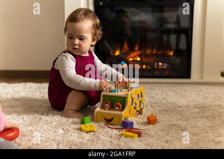 infanzia, sviluppo, abilità, giochi di motilità - piccolo bambino autentico bambina bambina compone specie forme colorate giocando legno giocattolo smistatore auto Foto Stock