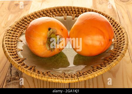 Due dolci persimmons naturali in una piastra di ceramica, primo piano, su un tavolo di legno. Foto Stock