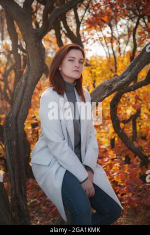 Una bella donna con testa rossa in buoni spiriti posa in un giorno d'autunno, godendo il bel tempo. Il concetto e l'idea di godersi la vacanza autunnale e autunnale Foto Stock