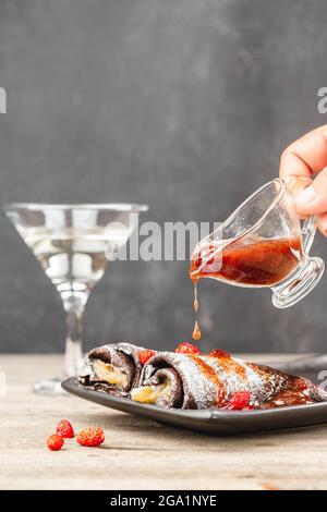 Versare la marmellata di fragole su panini sottili. Frittelle marroni panini versato marmellata di frutti di bosco e decorato fragole fresche. Foto Stock