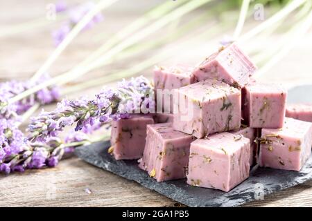 Piatto di formaggio lavanda con fiori secchi di lavanda su tavolo grigio di legno, vista dall'alto. Cubetti di formaggio porpora con ingredienti a base di erbe Foto Stock