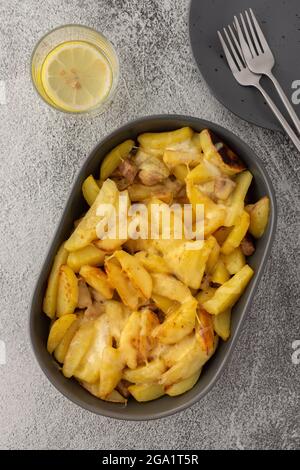 Stufati patate giovani con carne e formaggio in un piatto ovale, acqua di limone in un bicchiere, vista dall'alto Foto Stock