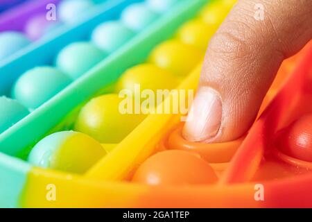Macro di mani con Pop IT sensoriale anti-stress. Kid play colorato arcobaleno pop it sensoriale giocattolo, mani da vicino. Concetto di pop IT gioco sensoriale per stres Foto Stock