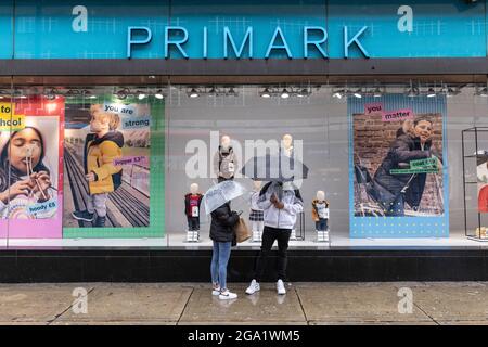 Gli acquirenti si trovano fuori da una filiale di "Primark" su Oxford Street sotto gli ombrelloni nelle forti docce a pioggia nel luglio 2021, Londra, Inghilterra, Regno Unito Foto Stock