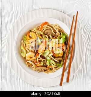Gamberi Yaki Udon, fritti in padella di udoni con gamberetti, cavolo, funghi di castagno, cipolla primaverile, carote, mirin e salsa di soia in ciotola bianca con costolette Foto Stock