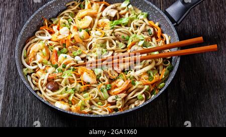 Gamberi Yaki Udon, fritti in padella di udoni con gamberetti, cavolo, funghi di castagno, cipolla primaverile, carote, mirin e salsa di soia in una padella con bastoncini Foto Stock