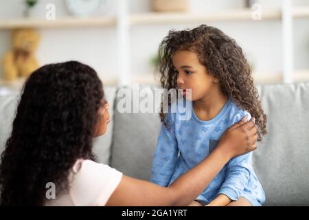 Mamma nera millenaria che sostiene la bambina arrabbiata e sconvolta, consolandola a casa. Conflitti familiari Foto Stock