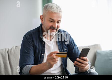 Uomo anziano felice che paga per i beni e i servizi in linea Foto Stock