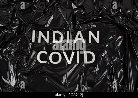 parole indian covid con lettere in metallo argentato sullo sfondo di una busta di plastica nera schiacciata Foto Stock