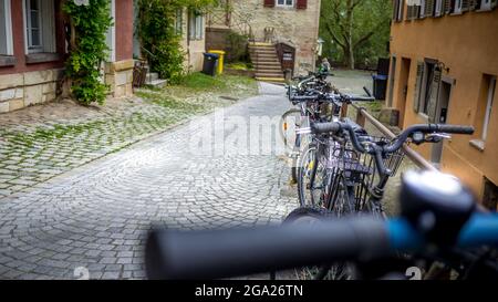 Una fila di biciclette parcheggiate lungo una strada lastricata in discesa nel centro storico. Giorno libero di cura. Foto Stock