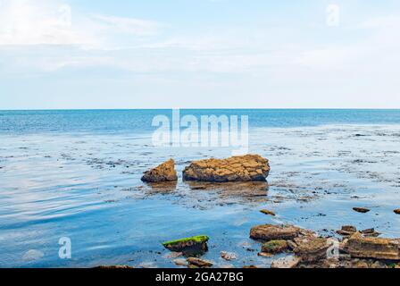 Il mare blu ancora glassy vibrante in Swanage Bay con rocce brune erose e screpolate erose appena fuori costa Foto Stock