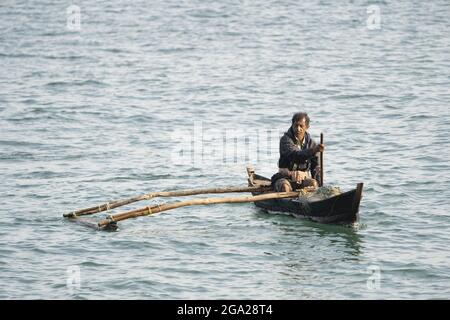 Uomo che paddling Outrigger canoa nel porto di Panjim, Goa, India Foto Stock