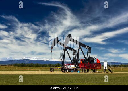 Due jack pompa in un campo verde con le nubi drammatiche e cielo blu sullo sfondo e neve gamma di montagna in lontananza, a ovest di ... Foto Stock