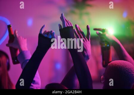 Alzò le braccia di giovani amici interculturali che ballano a casa festeggiamenti e bevande contro le luci rosa durante il fine settimana Foto Stock