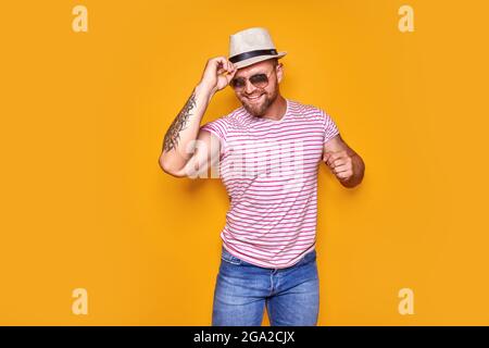 Ritratto di ottimista funky ragazzo danza indossare estate look cappello di paglia, occhiali da sole isolato su sfondo giallo Foto Stock