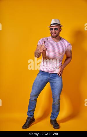 Ritratto di ottimista funky ragazzo danza indossare estate look cappello di paglia, occhiali da sole isolato su sfondo giallo Foto Stock