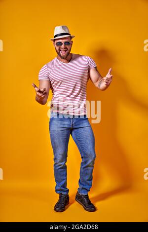 Ritratto di ottimista funky ragazzo danza indossare estate look cappello di paglia, occhiali da sole isolato su sfondo giallo Foto Stock