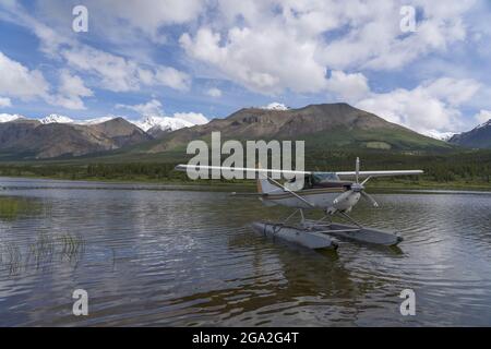 Idrovolante sull'acqua che riposa vicino alla riva di un lago con montagne sullo sfondo; Parco Nazionale e Riserva Kluane, Yukon, Canada Foto Stock