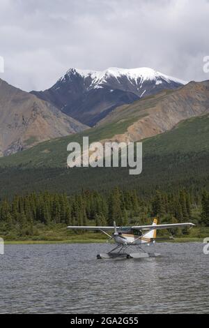 Idrovolante sull'acqua che riposa vicino alla riva di un lago con montagne boscose e innevate sullo sfondo Foto Stock