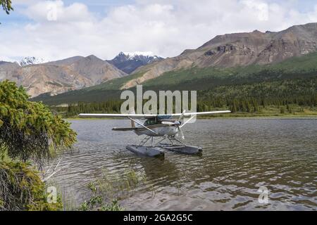 Idrovolante sull'acqua che riposa vicino alla riva di un lago con montagne sullo sfondo; Parco Nazionale e Riserva Kluane, Yukon, Canada Foto Stock