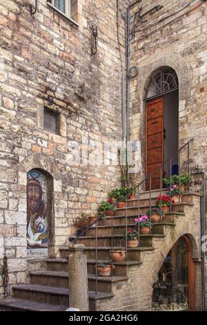 Scale e porta di un antico edificio in pietra con vasi colorati di fiori che fiancheggiano i gradini; Volterra, Provincia di Pisa, Toscana, Italia Foto Stock