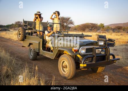Donne in una jeep, uno utilizzando binocoli e uno utilizzando una macchina fotografica, guardando nella savana con un conducente seduto al volante, mentre in safari al ... Foto Stock