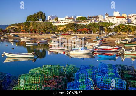 Piccole barche a motore ormeggiate lungo la spiaggia con colorate trappole da pesca accatastate sulla riva con edifici imbiancati sullo sfondo Foto Stock