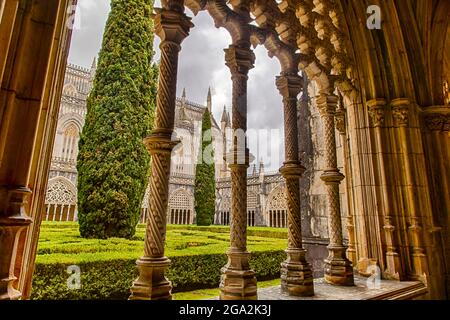 Guardando fuori attraverso le colonne ornate del chiostro nel giardino formale del cortile interno verso la cappella del monastero medievale o... Foto Stock