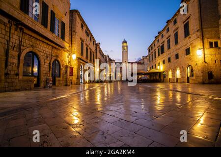 La luce si riflette sulle piastrelle di pietra di Piazza Luza nella Città Vecchia, guardando giù alla Torre dell'Orologio contro il cielo crepuscolo; Dubrovnik, Dalmazia, Croazia Foto Stock