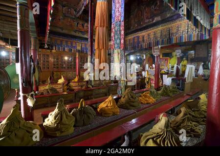 Abiti monastici accatastati in file su panchine nella Sala di preghiera al Monastero di Likir, sulle montagne Himalayane di Lakakh, Jammu e Kshmir Foto Stock