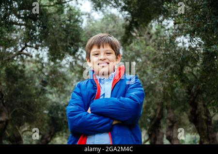 Ritratto di ragazzo in piedi con le braccia incrociate nel parco. Foto Stock