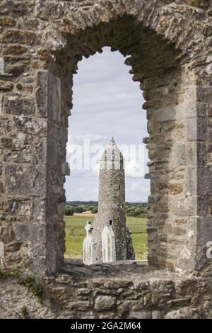 Guardando attraverso una finestra di lancetta alle rovine monastiche di Clonmacnoise alle pietre del cimitero e della McCarthy's Tower, le rovine del Tempio F... Foto Stock