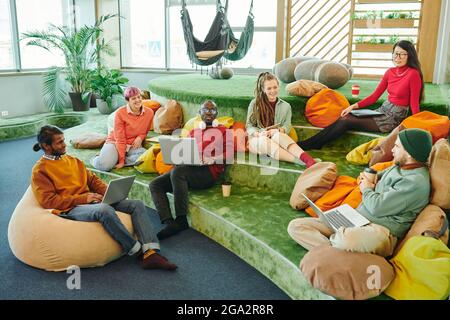 Felici i giovani dirigenti interculturali di un grande ufficio open space contemporaneo brainstorming e discutere di nuove idee alla riunione iniziale Foto Stock