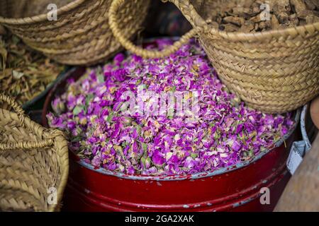 Primo piano del contenitore metallico con petali di rosa secchi e cesti di spezie in vendita nel souk delle spezie nella Medina di Marrakech Foto Stock