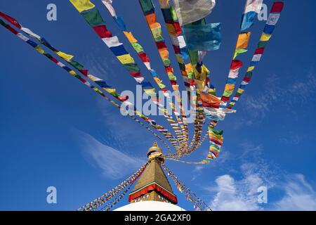 Bandiere di preghiera colorate appese alla guglia dorata del più grande stupa buddista tibetano in Nepal a Boudhanath superb di Kathmandu Foto Stock