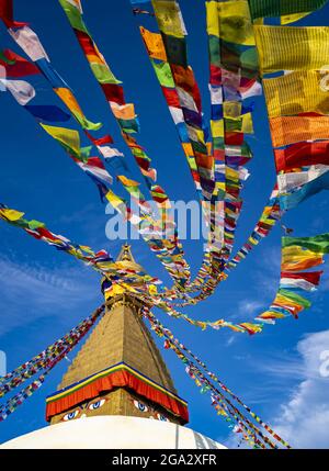 Bandiere di preghiera colorate appese alla guglia dorata del più grande stupa buddista tibetano in Nepal a Boudhanath superb di Kathmandu Foto Stock