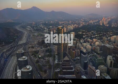 Vista serale su Santiago con il tramonto che riflette sul secondo grattacielo più alto del paese, Titanium la Portada e il fiume Mapocho RU... Foto Stock