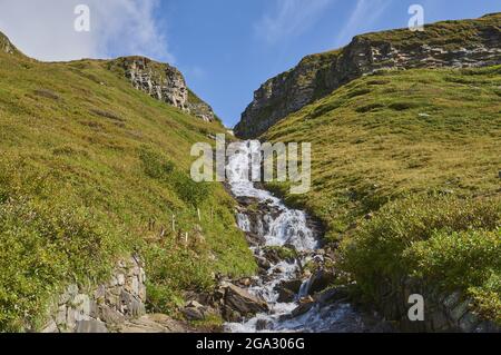 Cascata che scorre lungo la montagna erbosa al Hochalpenstraße (Hochalpenstrasse); Kärnten (Carinzia), Austria Foto Stock