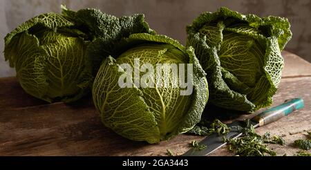 Teste di cavolo sabaudo sono disposte sul tavolo di legno con un coltello in una cucina rustica Foto Stock