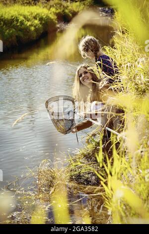 Una madre che trascorre del tempo all'aperto con la figlia e utilizza una rete per catturare insetti in un ruscello in un parco cittadino; Edmonton, Alberta, Canada Foto Stock