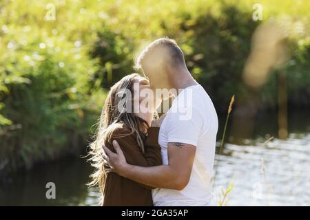 Marito e moglie trascorrono del tempo di qualità insieme e baciano all'aperto vicino a un ruscello in un parco cittadino; Edmonton, Alberta, Canada Foto Stock